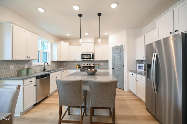 kitchen with appliances with stainless steel finishes, a kitchen island, light hardwood / wood-style flooring, white cabinetry, and hanging light fixtures