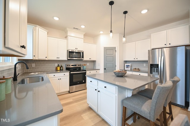 kitchen featuring sink, light wood-type flooring, a kitchen island, white cabinetry, and stainless steel appliances