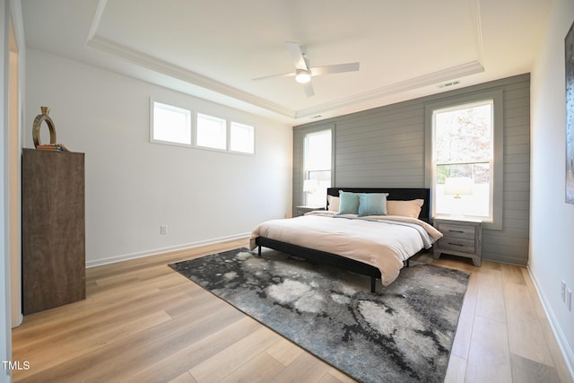 bedroom with light wood-type flooring, a raised ceiling, and ceiling fan