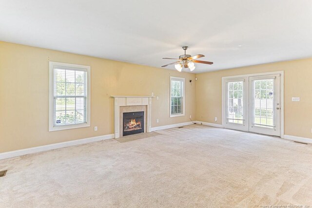 unfurnished living room with a tiled fireplace, light carpet, and a healthy amount of sunlight