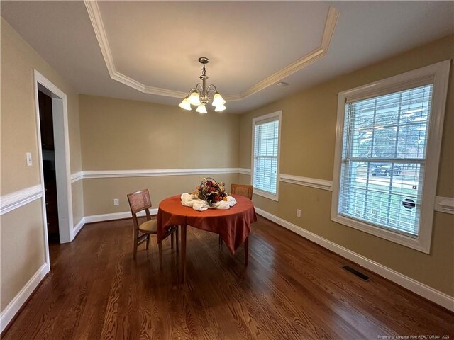 dining space with dark wood-type flooring, a chandelier, crown molding, and a raised ceiling