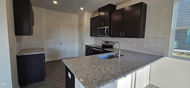 kitchen featuring sink, appliances with stainless steel finishes, kitchen peninsula, light stone countertops, and decorative backsplash