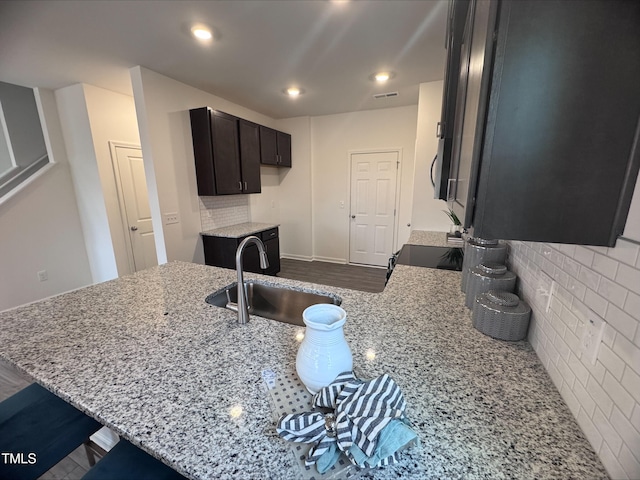 kitchen featuring tasteful backsplash, dark brown cabinets, sink, and light stone counters