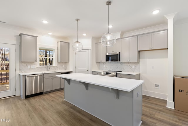 kitchen with decorative light fixtures, gray cabinets, a kitchen island, and appliances with stainless steel finishes