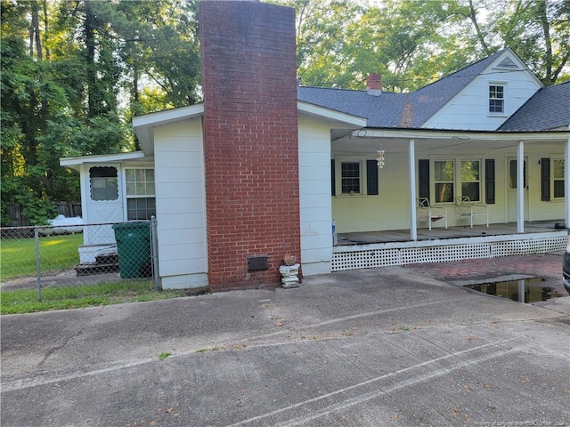 rear view of house featuring a chimney, covered porch, fence, and roof with shingles