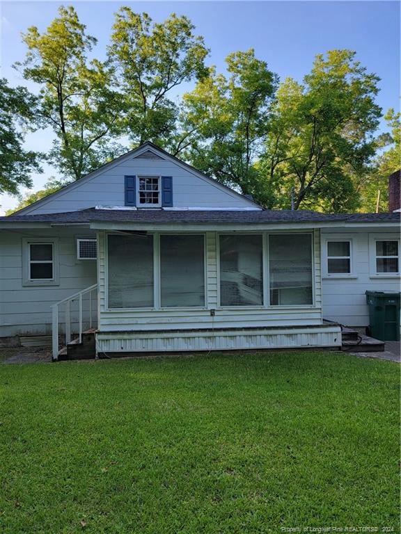 rear view of property with entry steps, roof with shingles, and a yard