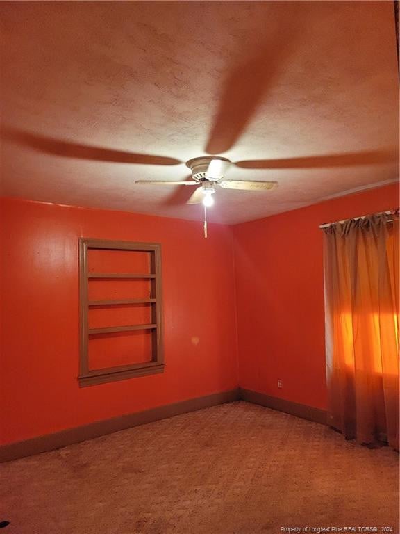 empty room with built in shelves, a textured ceiling, baseboards, ceiling fan, and carpet