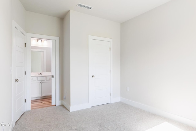 unfurnished bedroom with light colored carpet, baseboards, connected bathroom, and a sink