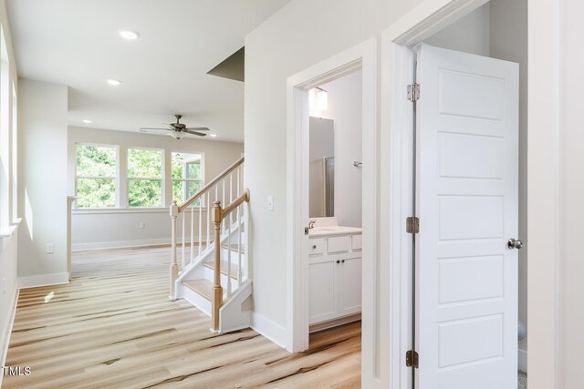corridor featuring light wood-style flooring, stairs, recessed lighting, baseboards, and a sink