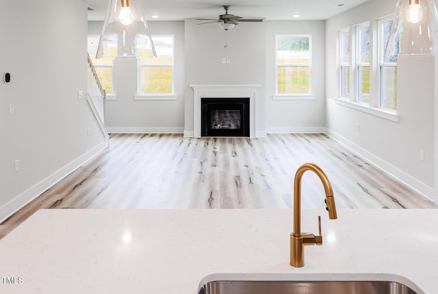 unfurnished living room featuring a sink, ceiling fan, wood finished floors, and baseboards