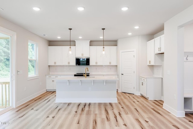 kitchen featuring light countertops, light wood-type flooring, decorative backsplash, white cabinetry, and a sink