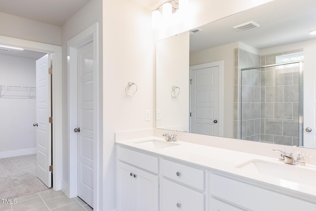 full bathroom featuring a tile shower, double vanity, a spacious closet, tile patterned flooring, and baseboards