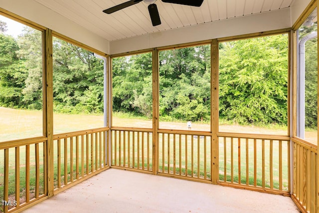 unfurnished sunroom featuring ceiling fan, healthy amount of natural light, and view of scattered trees