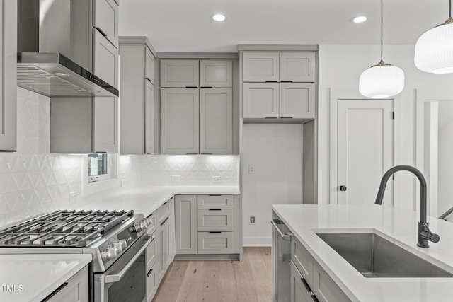 kitchen featuring wall chimney exhaust hood, appliances with stainless steel finishes, gray cabinets, light wood-type flooring, and a sink