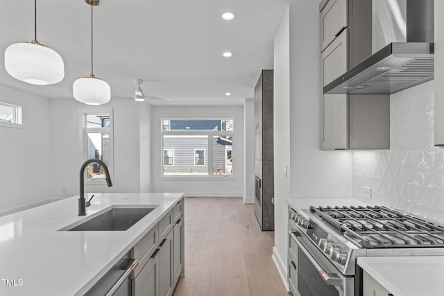 kitchen with a sink, light countertops, gray cabinets, stainless steel gas stove, and wall chimney exhaust hood