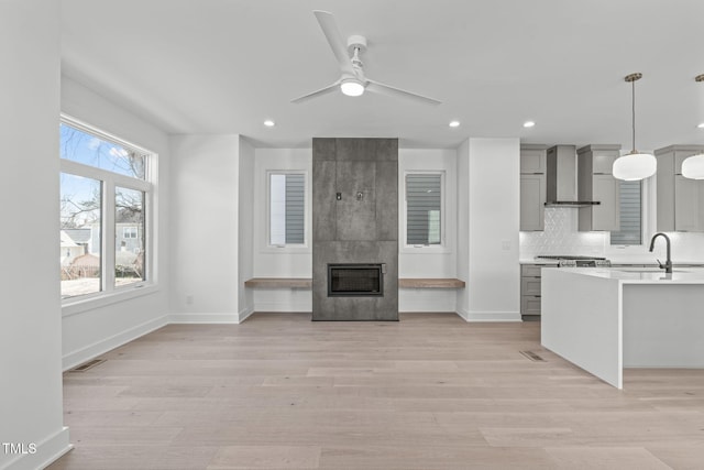 kitchen with gray cabinets, light countertops, a sink, a tile fireplace, and wall chimney exhaust hood