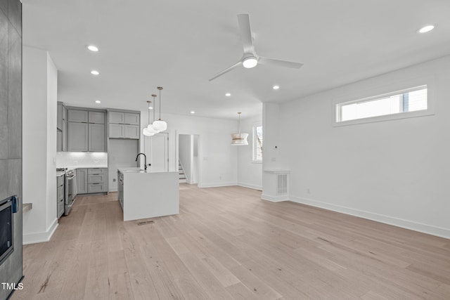 unfurnished living room featuring a ceiling fan, stairs, light wood-style floors, a sink, and recessed lighting