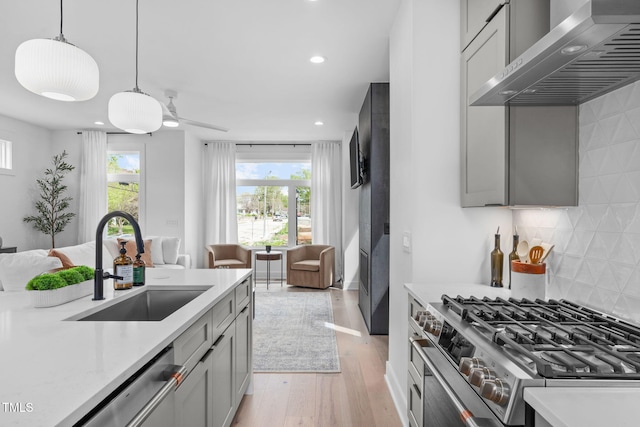 kitchen featuring stainless steel appliances, light countertops, wall chimney range hood, a sink, and open floor plan