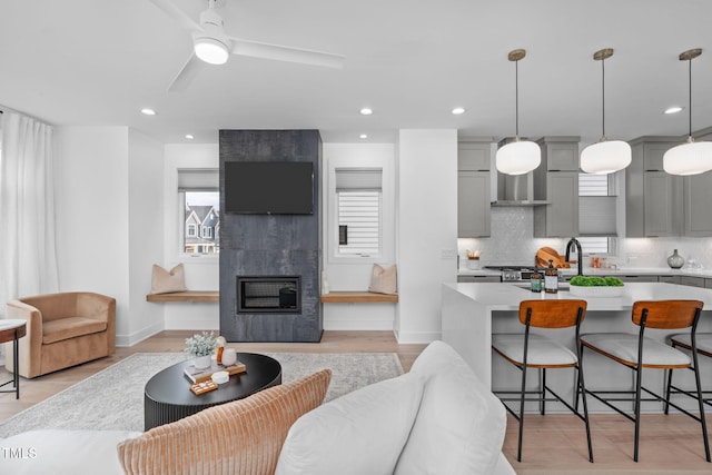 living area with recessed lighting, a fireplace, ceiling fan, light wood-type flooring, and baseboards