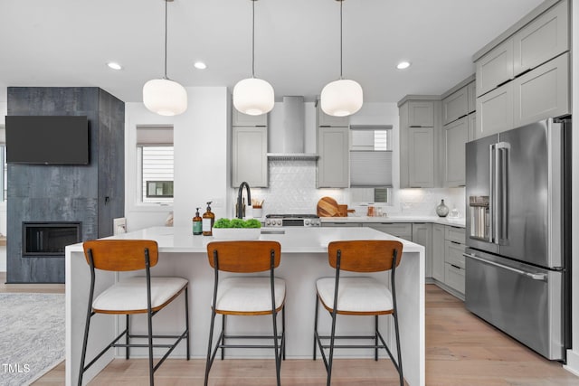 kitchen with light countertops, backsplash, high quality fridge, gray cabinetry, and wall chimney exhaust hood
