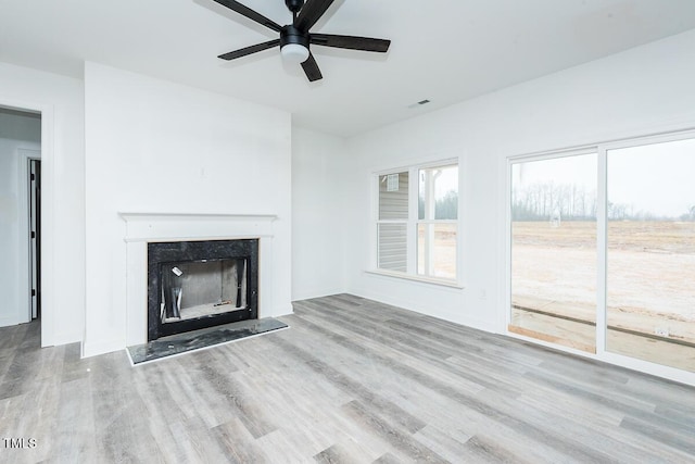 unfurnished living room with light wood-type flooring, a high end fireplace, visible vents, and ceiling fan