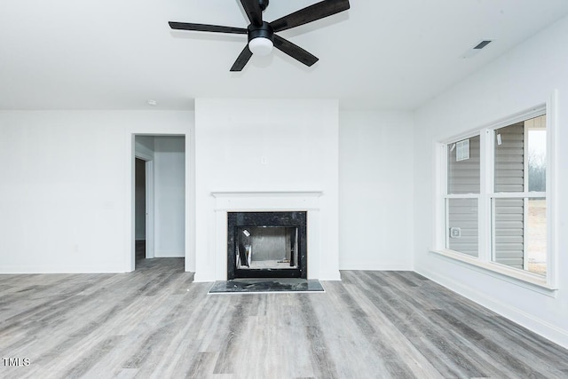 unfurnished living room featuring a high end fireplace, baseboards, ceiling fan, and light wood finished floors