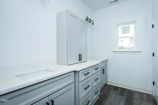 bathroom featuring wood finished floors, visible vents, baseboards, and double vanity