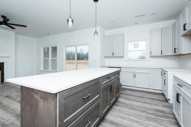 kitchen featuring wood finished floors, a kitchen island, a ceiling fan, light countertops, and decorative light fixtures