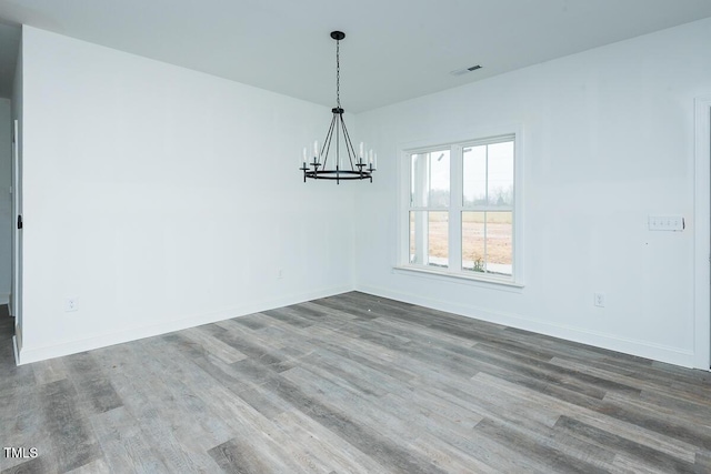 empty room with baseboards, wood finished floors, visible vents, and an inviting chandelier