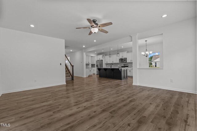 unfurnished living room with dark wood-type flooring and ceiling fan with notable chandelier