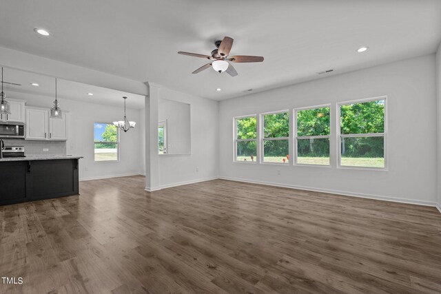 unfurnished living room with plenty of natural light, ceiling fan with notable chandelier, and hardwood / wood-style flooring