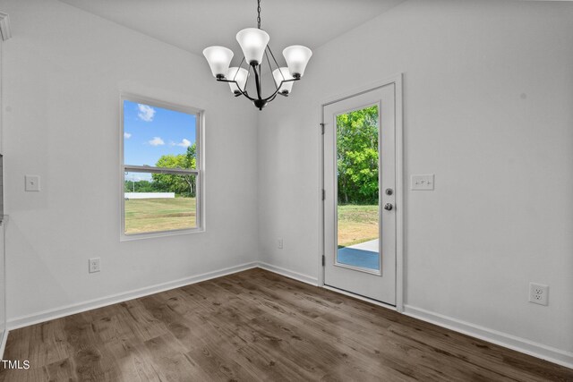 unfurnished dining area featuring dark wood-type flooring, a notable chandelier, and plenty of natural light