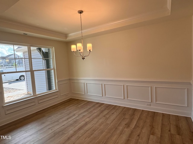 spare room with an inviting chandelier, ornamental molding, a tray ceiling, and light hardwood / wood-style flooring