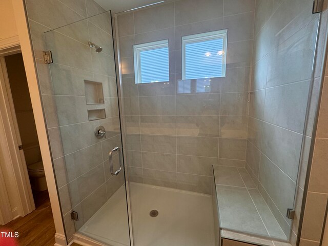 bathroom with wood-type flooring, a shower with shower door, and toilet