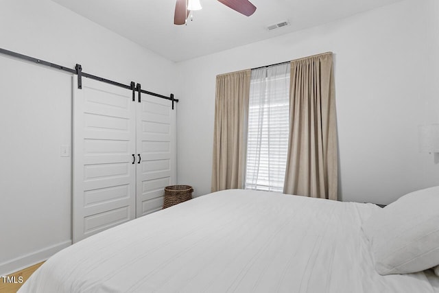 bedroom featuring a barn door, ceiling fan, a closet, and hardwood / wood-style floors