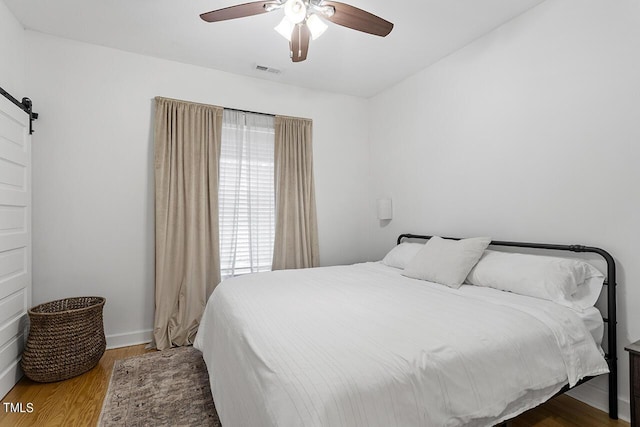 bedroom with hardwood / wood-style floors, ceiling fan, and a barn door