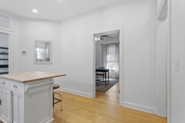 interior space featuring a kitchen breakfast bar, light wood-type flooring, ceiling fan, white cabinetry, and butcher block counters