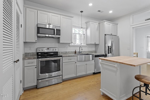 kitchen featuring light hardwood / wood-style floors, stainless steel appliances, sink, butcher block countertops, and a breakfast bar area