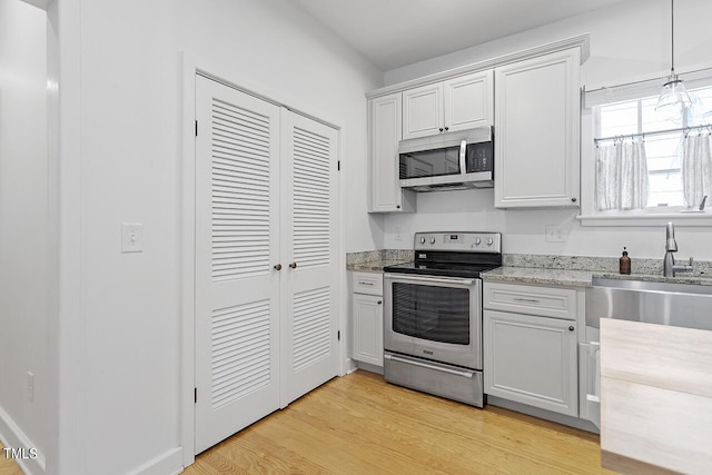 kitchen with decorative light fixtures, white cabinetry, appliances with stainless steel finishes, and light hardwood / wood-style flooring