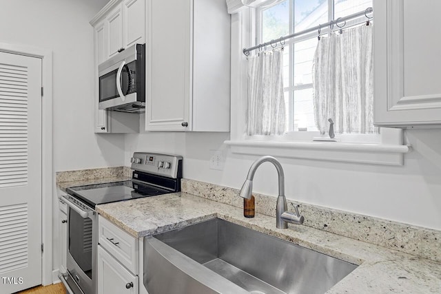 kitchen with light stone counters, sink, white cabinetry, and stainless steel appliances