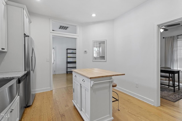 kitchen with wood counters, white cabinets, light hardwood / wood-style floors, a kitchen bar, and stainless steel appliances