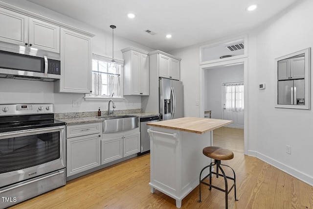 kitchen with appliances with stainless steel finishes, sink, light hardwood / wood-style flooring, hanging light fixtures, and butcher block counters