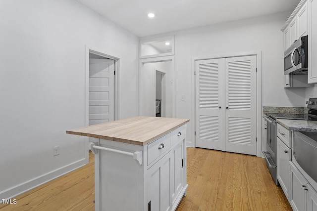 kitchen with white cabinets, stainless steel appliances, a kitchen island, and butcher block counters