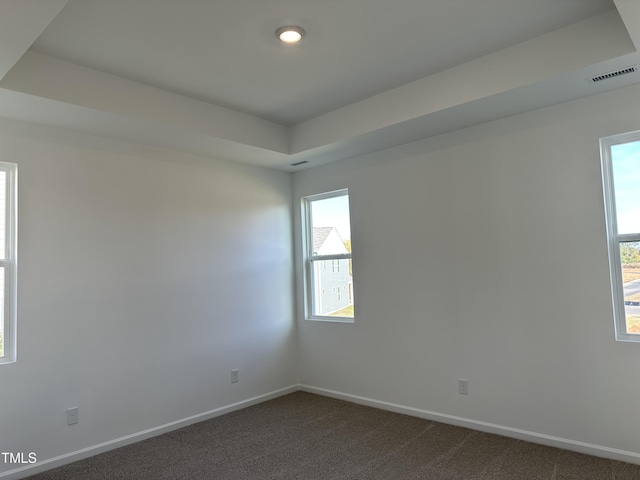 unfurnished room with visible vents, baseboards, dark carpet, and a raised ceiling
