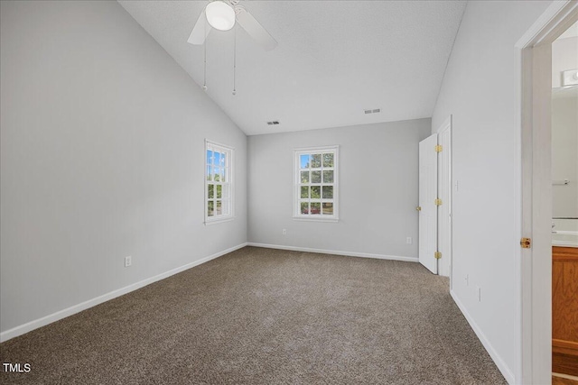 carpeted spare room featuring ceiling fan, visible vents, baseboards, and vaulted ceiling