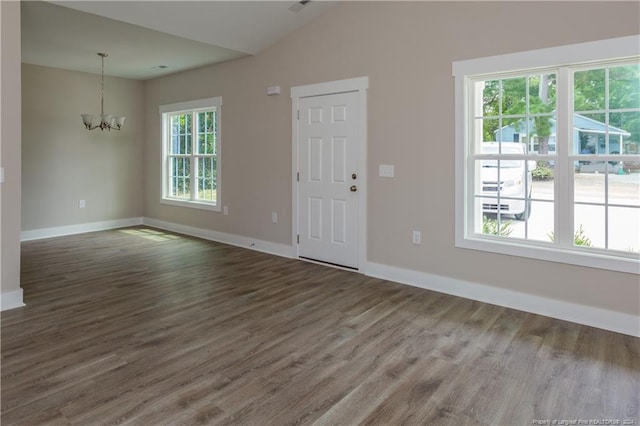 foyer entrance with baseboards, a chandelier, vaulted ceiling, and wood finished floors