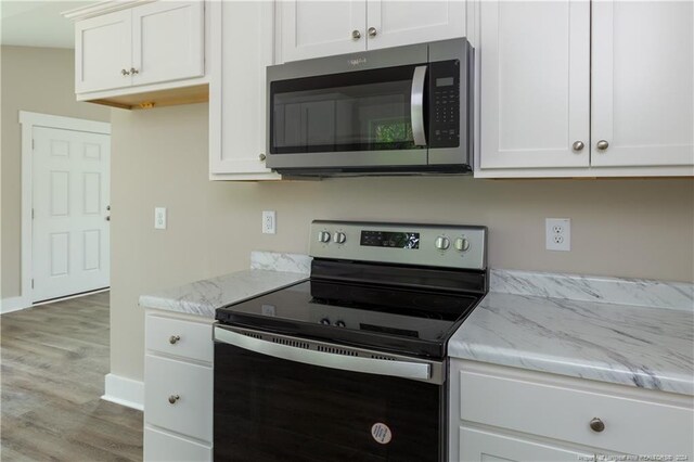 kitchen featuring appliances with stainless steel finishes, light hardwood / wood-style flooring, light stone counters, and white cabinets