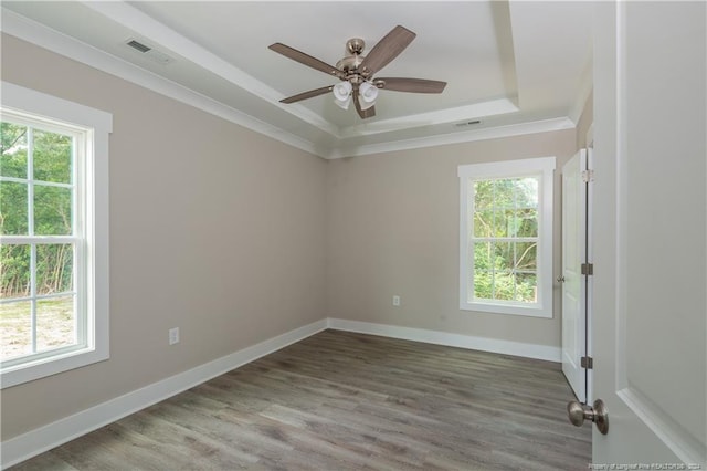 spare room with a raised ceiling, visible vents, ornamental molding, wood finished floors, and baseboards