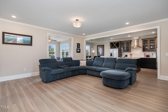 living room with bar area, ceiling fan, light hardwood / wood-style floors, and ornamental molding