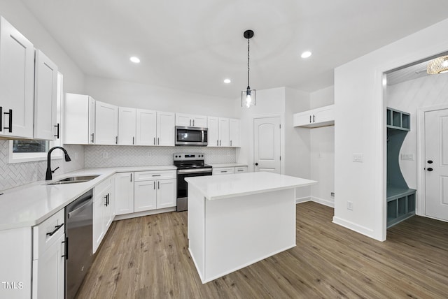 kitchen with hardwood / wood-style floors, white cabinets, a center island, decorative light fixtures, and stainless steel appliances